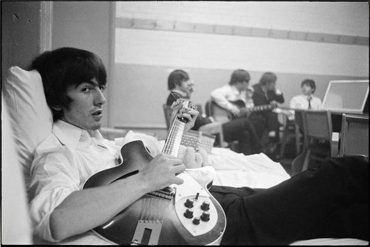 George Harrison on the bed with guitar, 1964 by Curt Gunther